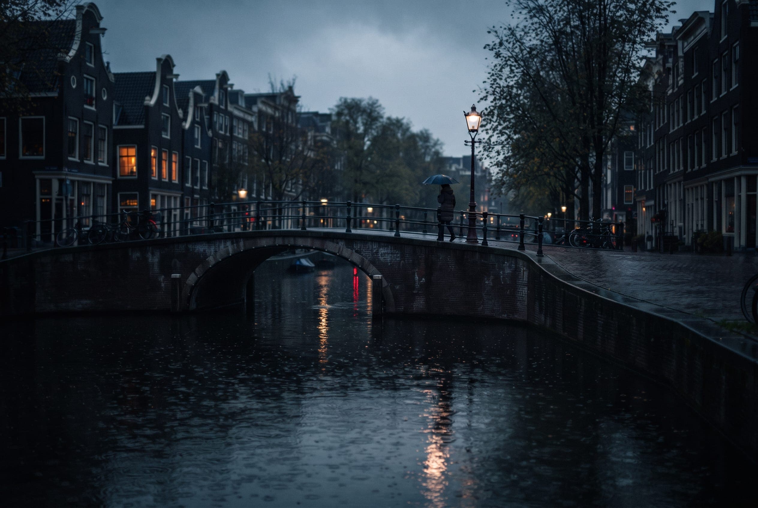 Rain pitting black canal water at dusk, lamplight smeared into long reflections beneath an arched bridge.